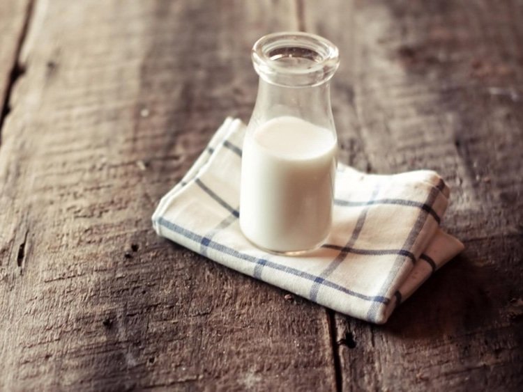 Goat-Milk-fort-collins Glass bottle of fresh milk on a checkered cloth napkin placed on a rustic wooden table.